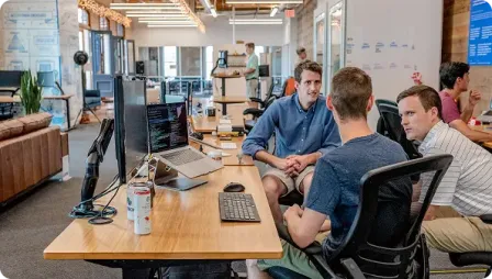 Team members discussing code at desk in open office.