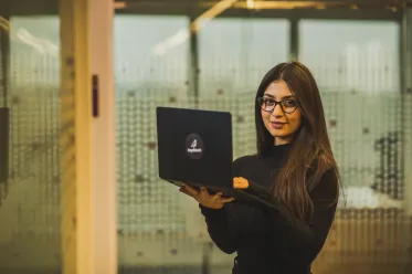 Associate holding branded laptop in office hallway.