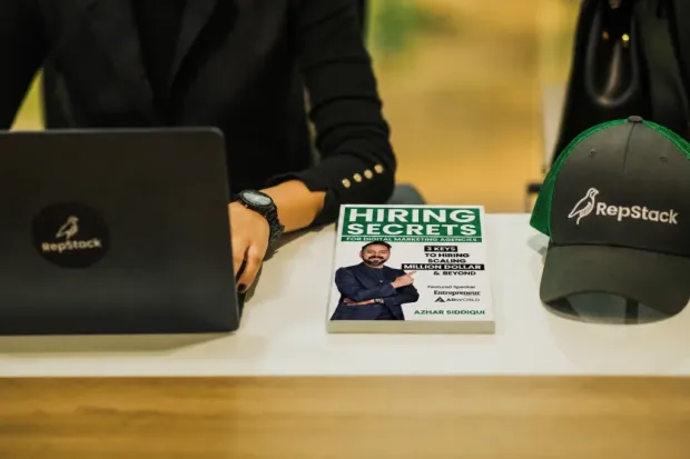 RepStack branded laptop, cap, and 'Hiring Secrets' book on desk